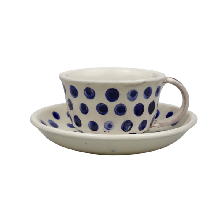Ceramic cup with blue polka dots and matching saucer on a light gray background