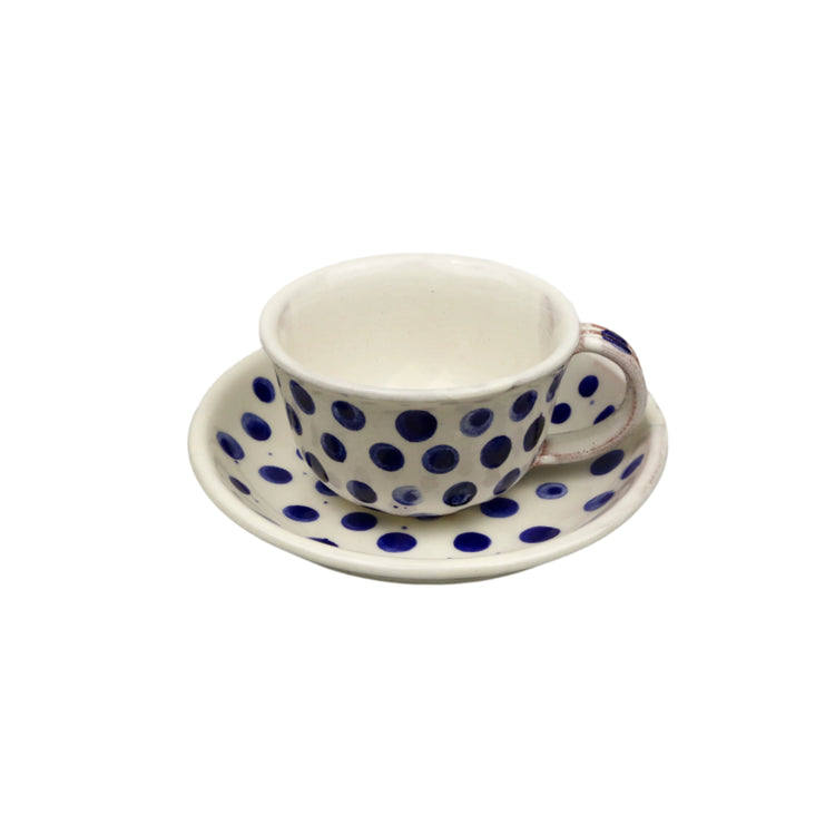 Ceramic cup with blue polka dots on a matching saucer against a gray background