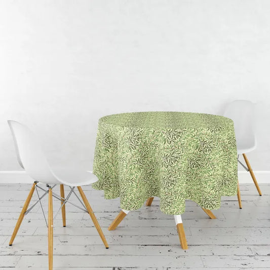 Green patterned tablecloth on a round table with white chairs in a room with a white wall and wooden floor.