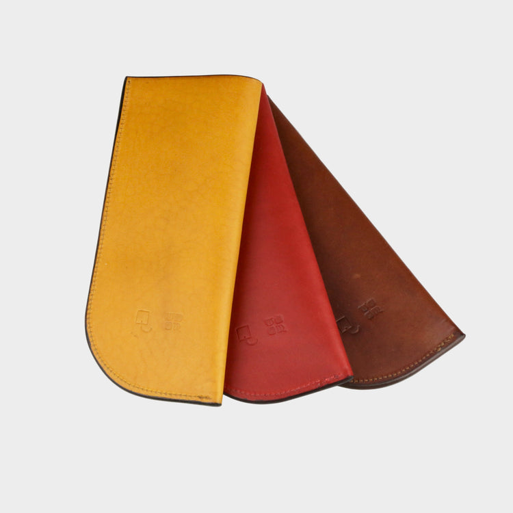 Three leather pouches in yellow, red, and brown on a light gray background