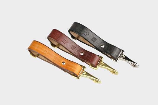 Three leather straps in different colors with gold hardware on a light gray background