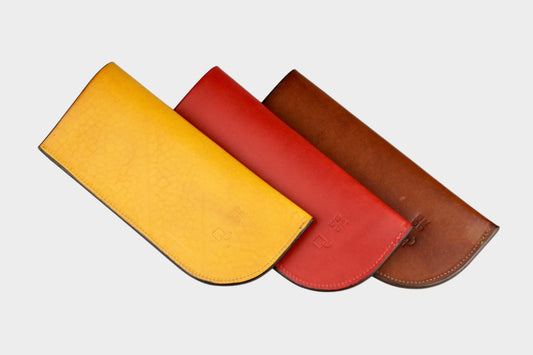 Three leather cases in yellow, red, and brown on a light gray background