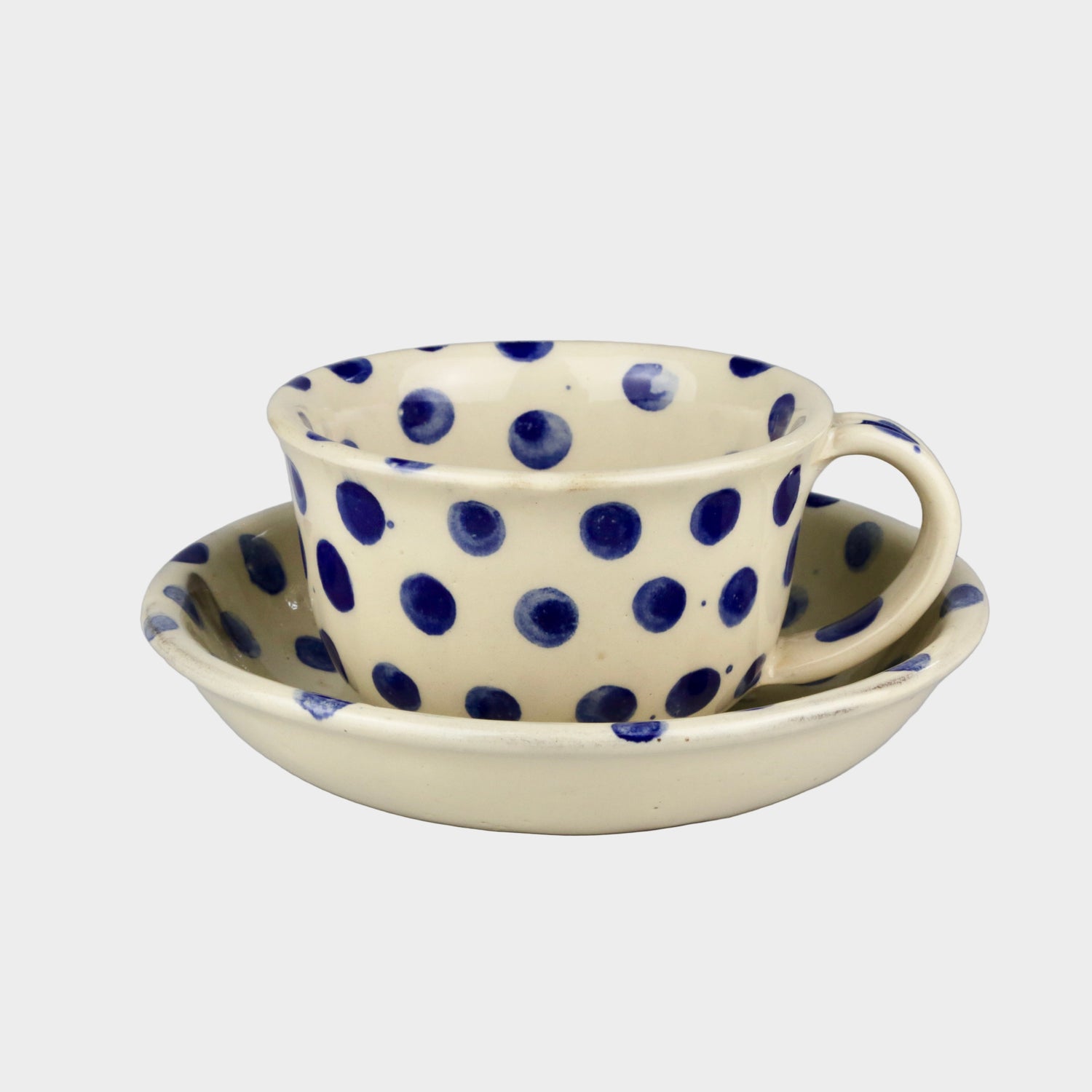 Ceramic cup and saucer set with blue polka dots on a gray background