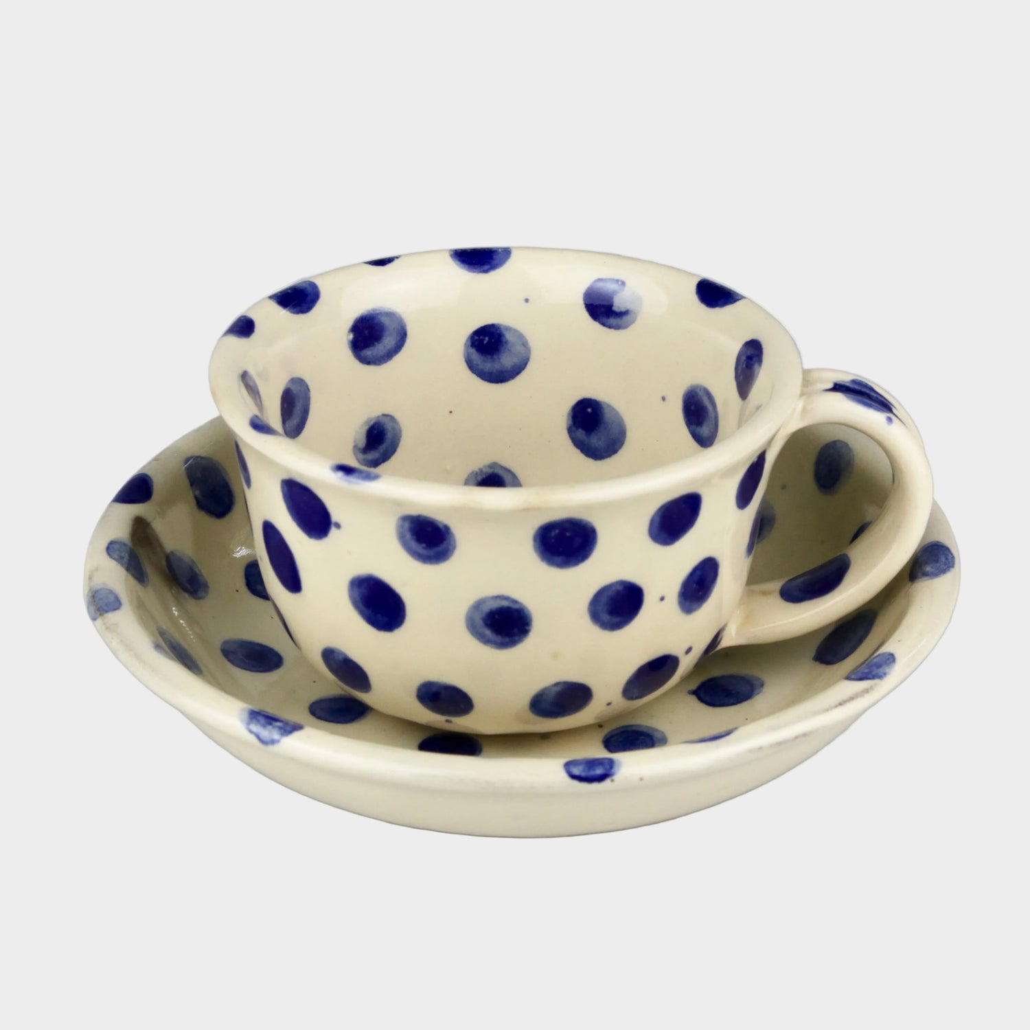 Ceramic cup and saucer set with blue polka dots on a gray background