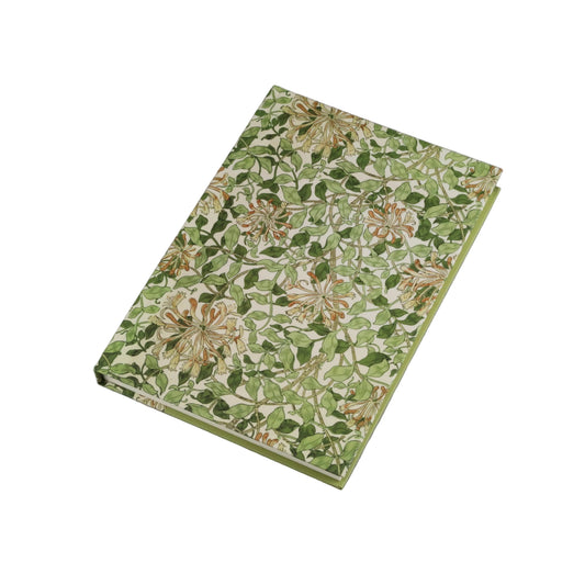 A rectangular notebook or journal with a green and beige floral patterned cover, photographed at an angle on a neutral gray background.