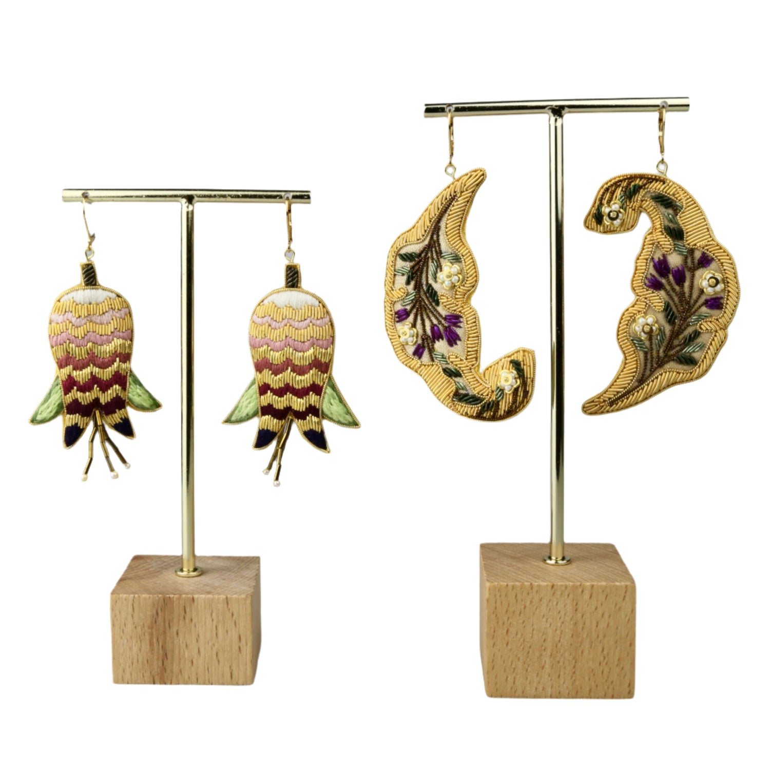 Pair of embroidered earrings on gold stands with wooden bases against a gray background