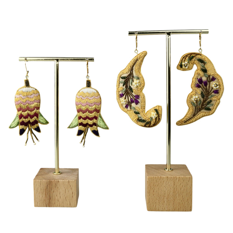 Pair of embroidered earrings on gold stands with wooden bases against a gray background