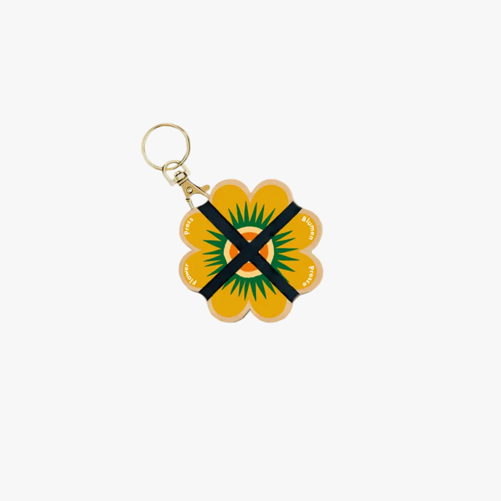 Flower-shaped keychain with a black and green design on a beige background
